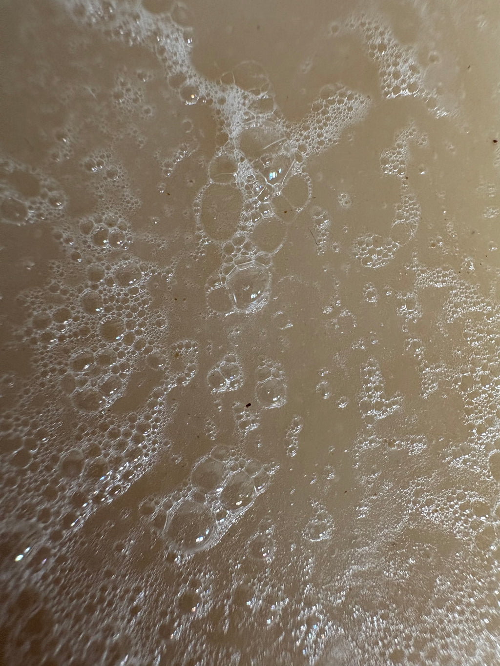 A close-up texture shot of a light beige soil soap with dense white foam and bubbles across the surface.
